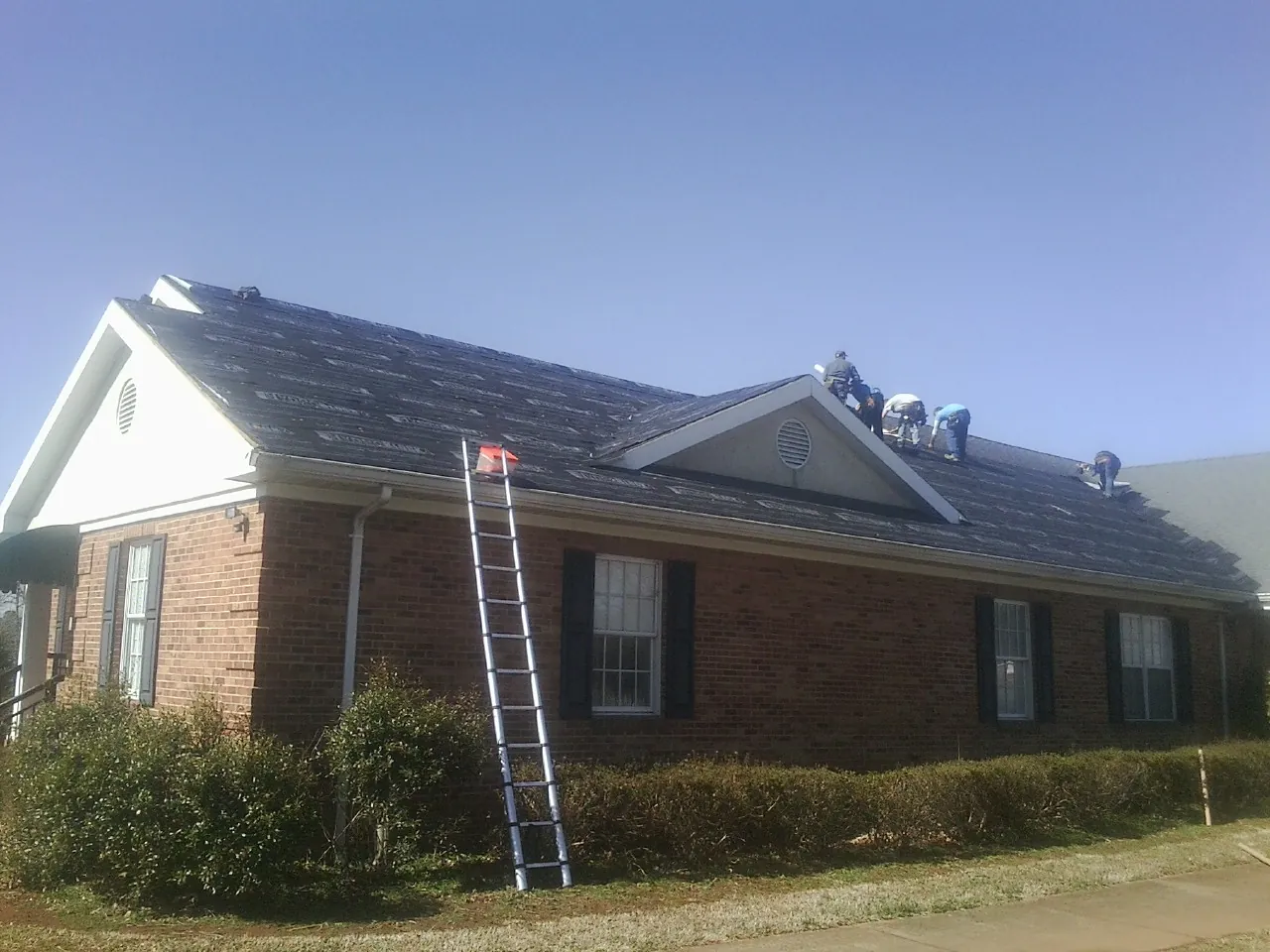 Crew tearing shingles off a brick ranch roof with a ladder set — Metal Roof Repair work by our crew in Brunswick