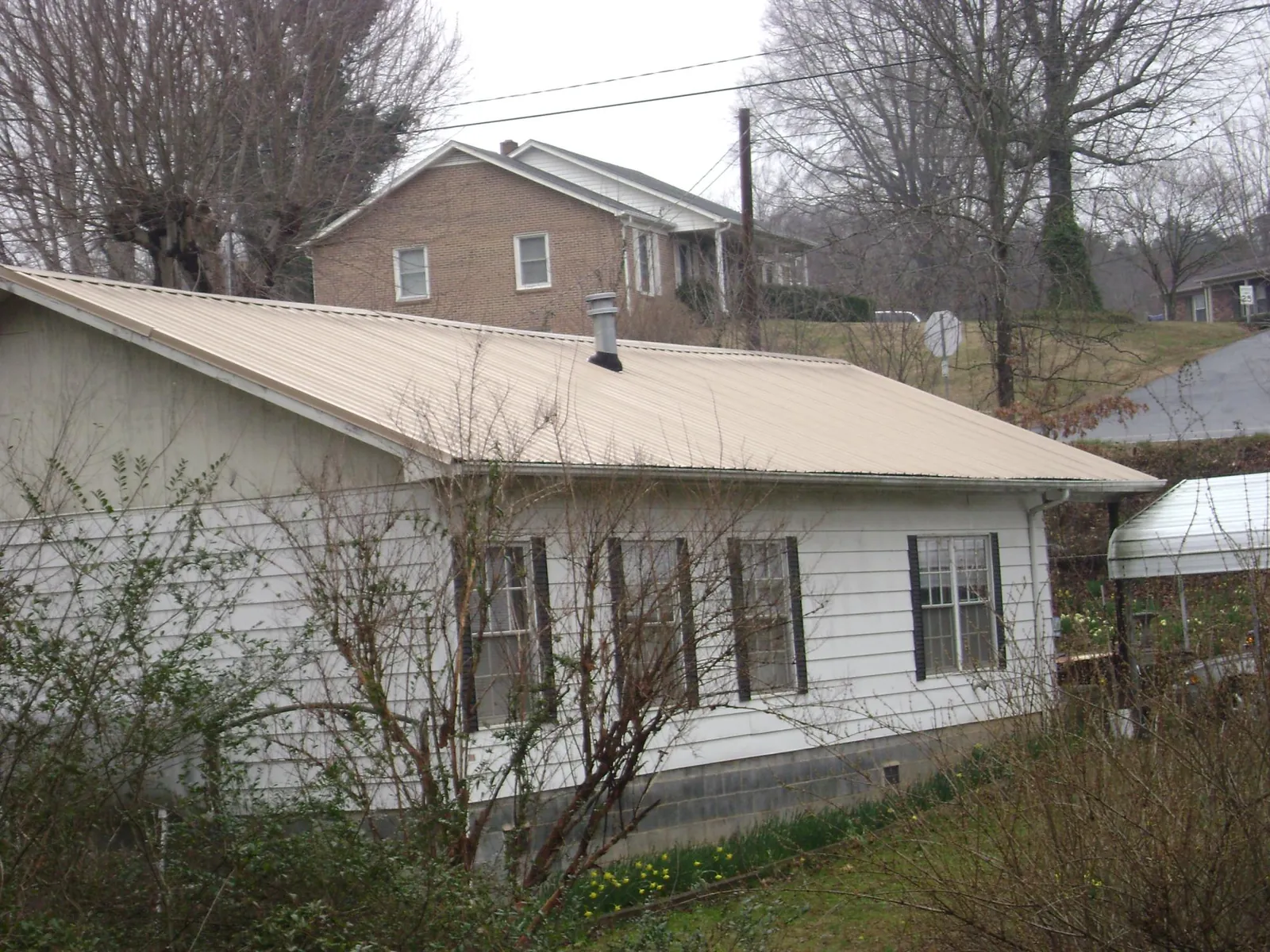 Tan metal roof on a white sided house set into a hillside — Commercial Roofing by Roofing Brothers in Brunswick